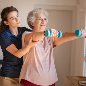 A medical professional assists an elderly woman with an exercise using two small dumbbells